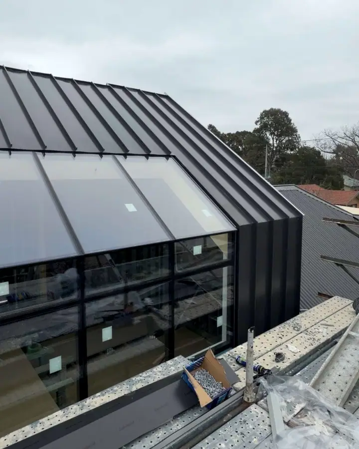 Dark standing seam metal running over the roof edge and down the wall beside a large glazed gable